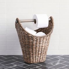 a wicker basket with two rolls of toilet paper in it on a tiled floor