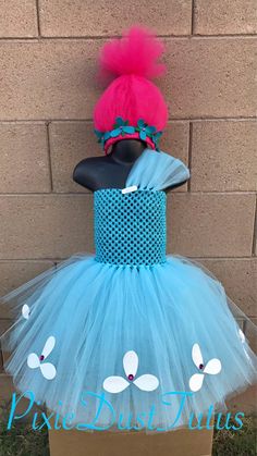 a dress made out of tulle and mesh with flowers on the top, sitting in front of a brick wall