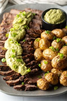 steak, potatoes and guacamole are on a plate with green garnish