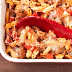 a casserole dish with sausage, tomatoes and pasta in it on a wooden table