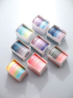 six different colors of washi tape in boxes on a white surface with one box open and the other closed