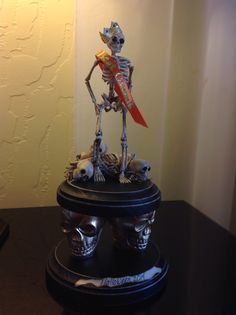 a skeleton figurine holding a red flag on top of a black table next to a lamp