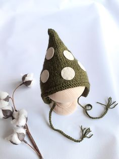 a green knitted hat with white polka dots on it next to cotton flowers and twigs