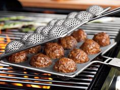 some meatballs are being cooked on a grill with tongs over them and another food item in the background