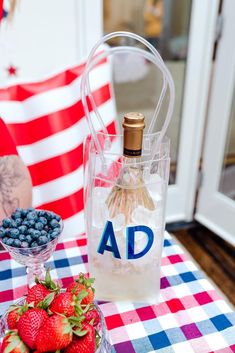 a bottle of ad next to strawberries and blueberries on a checkered tablecloth