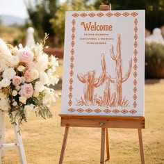 a welcome sign with flowers in the foreground and an easel on the ground