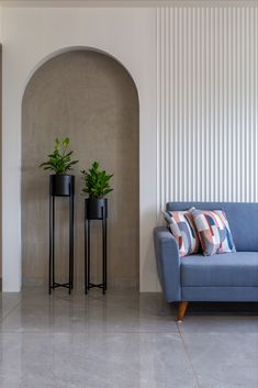 a blue couch sitting next to two planters on top of a white tiled floor