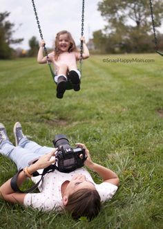 two children playing on swings in the grass, one holding a camera and the other taking pictures