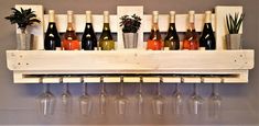 wine glasses and bottles are lined up on a wooden rack with succulents