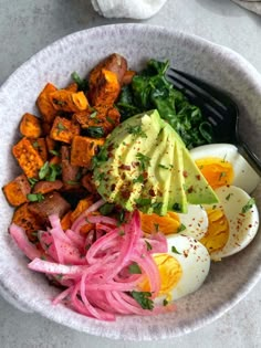 a bowl filled with vegetables and eggs on top of a white countertop next to a fork