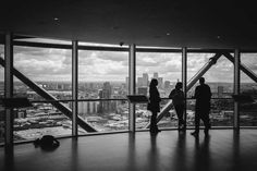 three people standing in front of large windows looking out at the city below and skyscrapers behind them