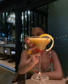 a woman sitting at a table with a drink in her hand and a lemon slice on the rim