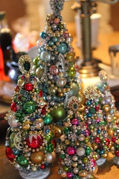 three small christmas trees made out of beads and other ornaments on a table with a lamp in the background