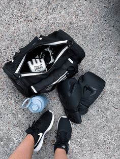 a person standing next to a duffel bag with shoes and water bottle in it