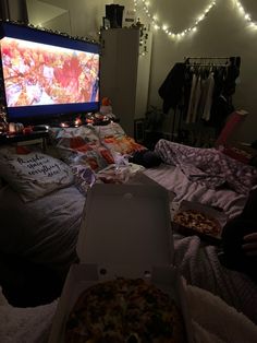 two pizzas sitting on top of a bed next to a flat screen tv in a bedroom