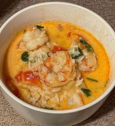 a white bowl filled with shrimp and grits next to a cup of soup on top of a table