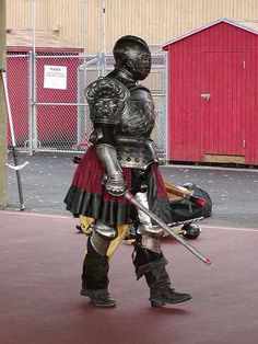 a man dressed in armor and holding a baseball bat standing on a court with a red building behind him