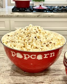 a red bowl filled with popcorn sitting on top of a kitchen counter next to an oven