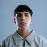 a young man with short black hair wearing a grey shirt and silver earrings