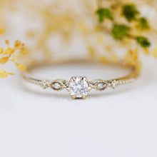 a white diamond ring sitting on top of a table next to flowers and greenery