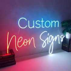 a neon sign that says custom neon signs on the wall next to a stack of books