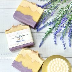 three bars of soap sitting on top of a wooden table next to purple and white flowers