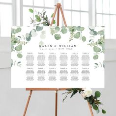 an easel with greenery and white flowers on it is holding a wedding seating chart