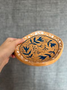 a hand holding a blue and white plate with leaves on it's side, in front of a gray background