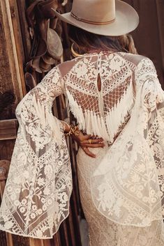 the back of a woman wearing a white lace dress and cowboy hat with her hands on her hips