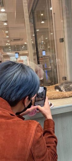 a woman with blue hair taking a photo in front of a cat behind a glass window