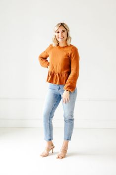 a woman standing in front of a white wall with her hands on her hips and smiling