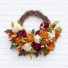 a wreath with autumn leaves and flowers hanging on a brick wall in front of a white brick wall