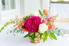 a vase filled with lots of flowers on top of a white table covered in greenery