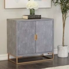 a gray cabinet sitting next to a vase with white flowers on it and a plant in the corner