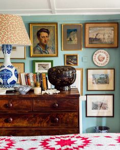 a bedroom with pictures on the wall and a dresser in front of it, along with a lamp