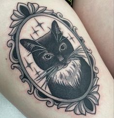 a black and white photo of a cat in a frame tattoo on the thigh with an ornate border around it