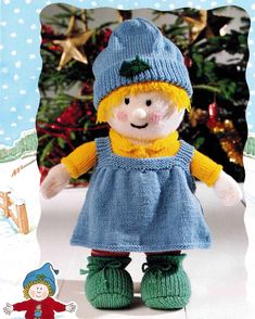 a knitted doll is standing in front of a christmas tree with snowflakes