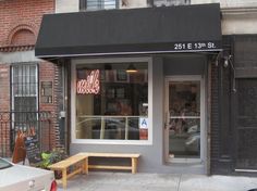 a store front with a wooden bench in front of it and cars parked on the street