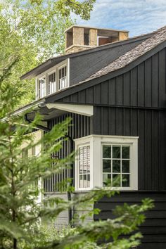 a black house with white trim and windows on the roof is surrounded by greenery