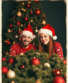 two people wearing santa hats sitting in front of a christmas tree