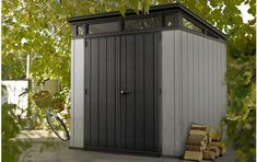 a small shed sitting next to a pile of logs under a tree with a bicycle leaning against it