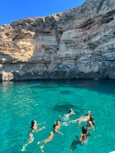 four people swimming in the water near some cliffs and blue water with rocks on either side