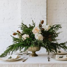 an arrangement of flowers and greenery in a vase on a table with place settings