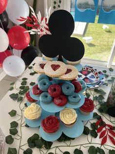 a mickey mouse cake with donuts and raspberries on top, surrounded by balloons