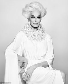 a black and white photo of a woman with blonde hair sitting on a chair wearing a fur collar