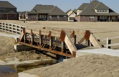 a wooden bridge over a small creek in front of some houses