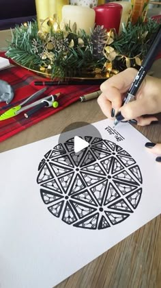 someone is drawing an apple with black and white ink on a piece of paper next to some christmas decorations