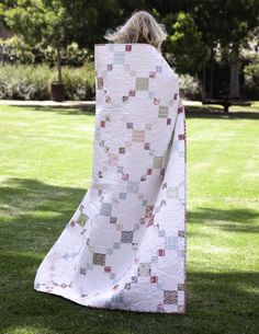 a woman standing in the grass with a quilt on her back and she is holding it up