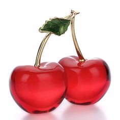 two shiny red cherries with green leaves on them, sitting side by side in front of a white background