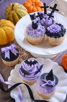 cupcakes decorated with purple frosting and black decorations on plates next to pumpkins